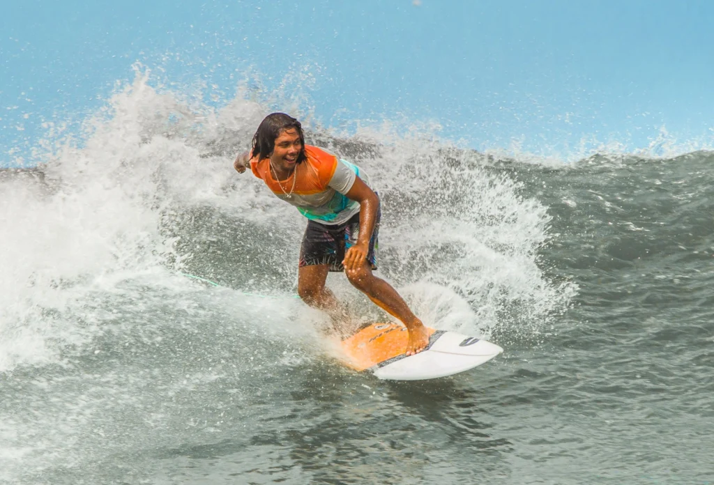 A huy surfing the waves of bali, standing on his surfboard and smiling