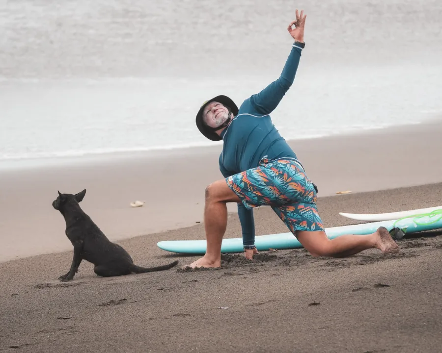 Surfer stretching on the beach before surfing - twoo surfboards next to him and a dog looking at the water